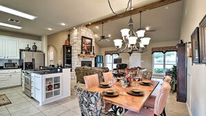 A spacious kitchen with white cabinets, a stone fireplace, and a dining area with striped chairs and a wooden table.