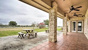 A covered patio area with stone pillars, picnic tables, and ceiling fans.