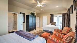 A hotel room with two beds, a ceiling fan, a dark wooden wardrobe, a large window with curtains, and a patterned rug.