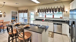 A modern kitchen with a central island, white cabinetry, stainless steel appliances, and a dining area with striped chairs.