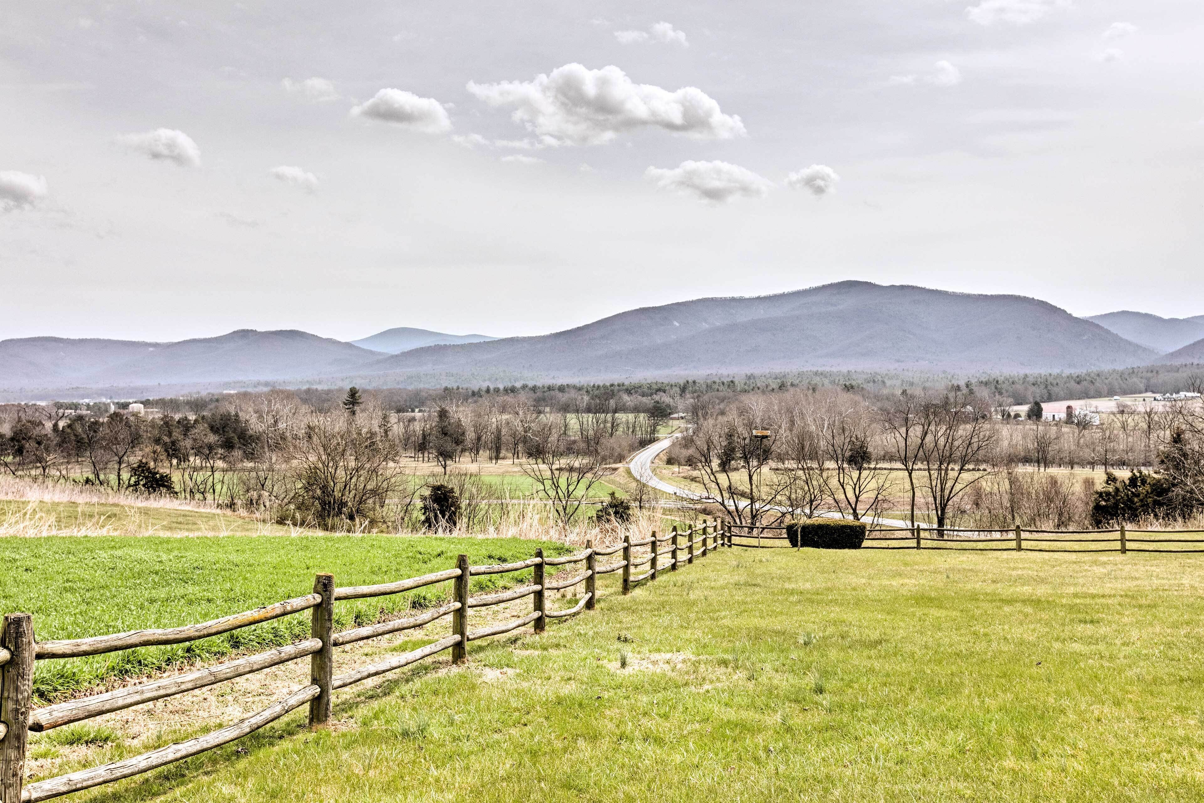 A rural landscape with a wooden fence, a winding road, and distant mountains.