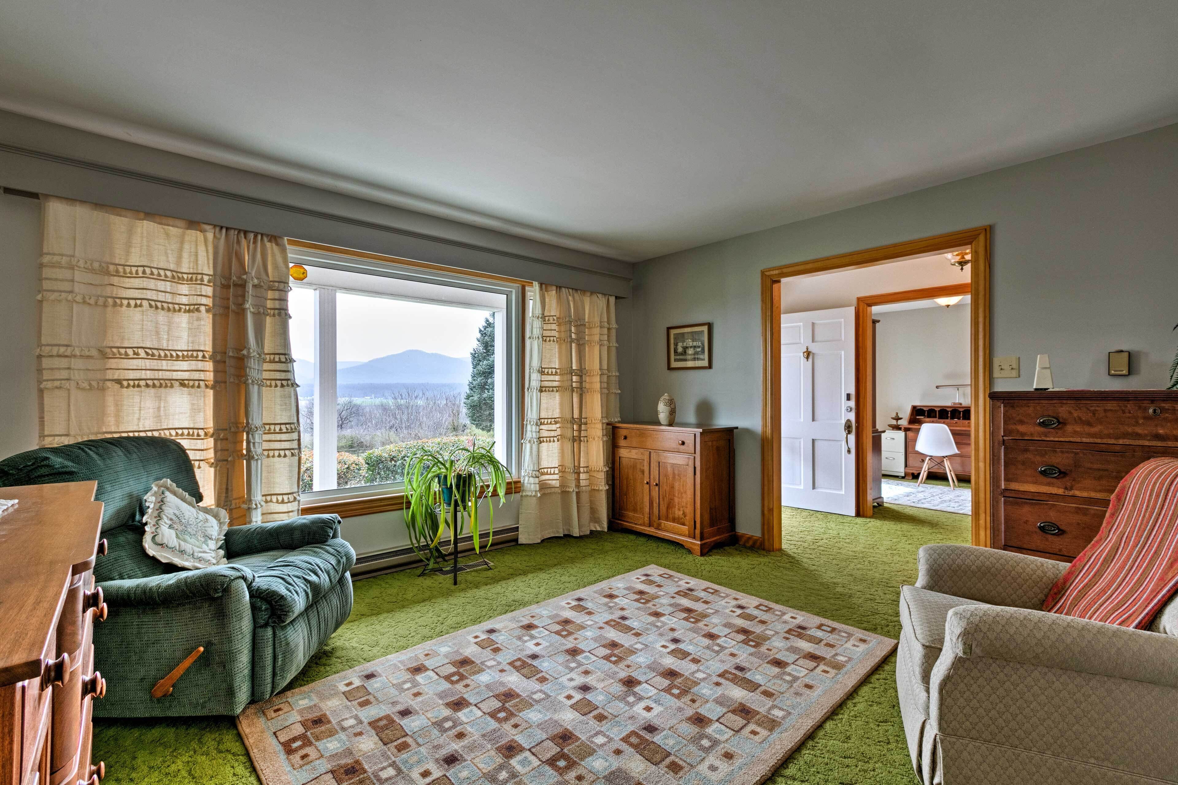 A cozy living room with a green sofa, a patterned rug, and a view of mountains through the window.