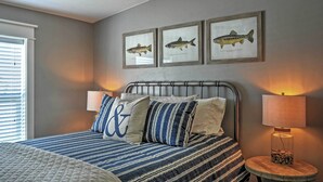 Une chambre à coucher comprenant un lit, deux lampes fixées au mur, une table de chevet avec une lampe, et trois tableaux représentant des poissons, accrochés au mur.