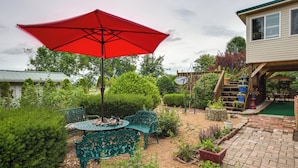 A patio area with a red umbrella, green metal chairs, and a small table.