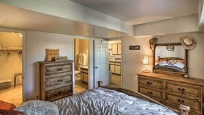 Een slaapkamer met een bed, een houten dressoir en een spiegel. Er is een deur naar een badkamer en een keuken.