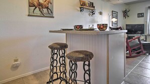 Een keuken met een bar, krukken, een schilderij en een televisie.