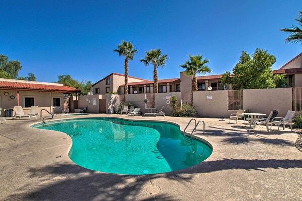 A swimming pool with lounge chairs and palm trees, surrounded by buildings with red roofs.