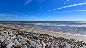 A rocky beach with waves crashing onto the shore under a clear blue sky. - 2 Blocks to Surfside Beach: A-frame Home w/ Deck (Freeport)