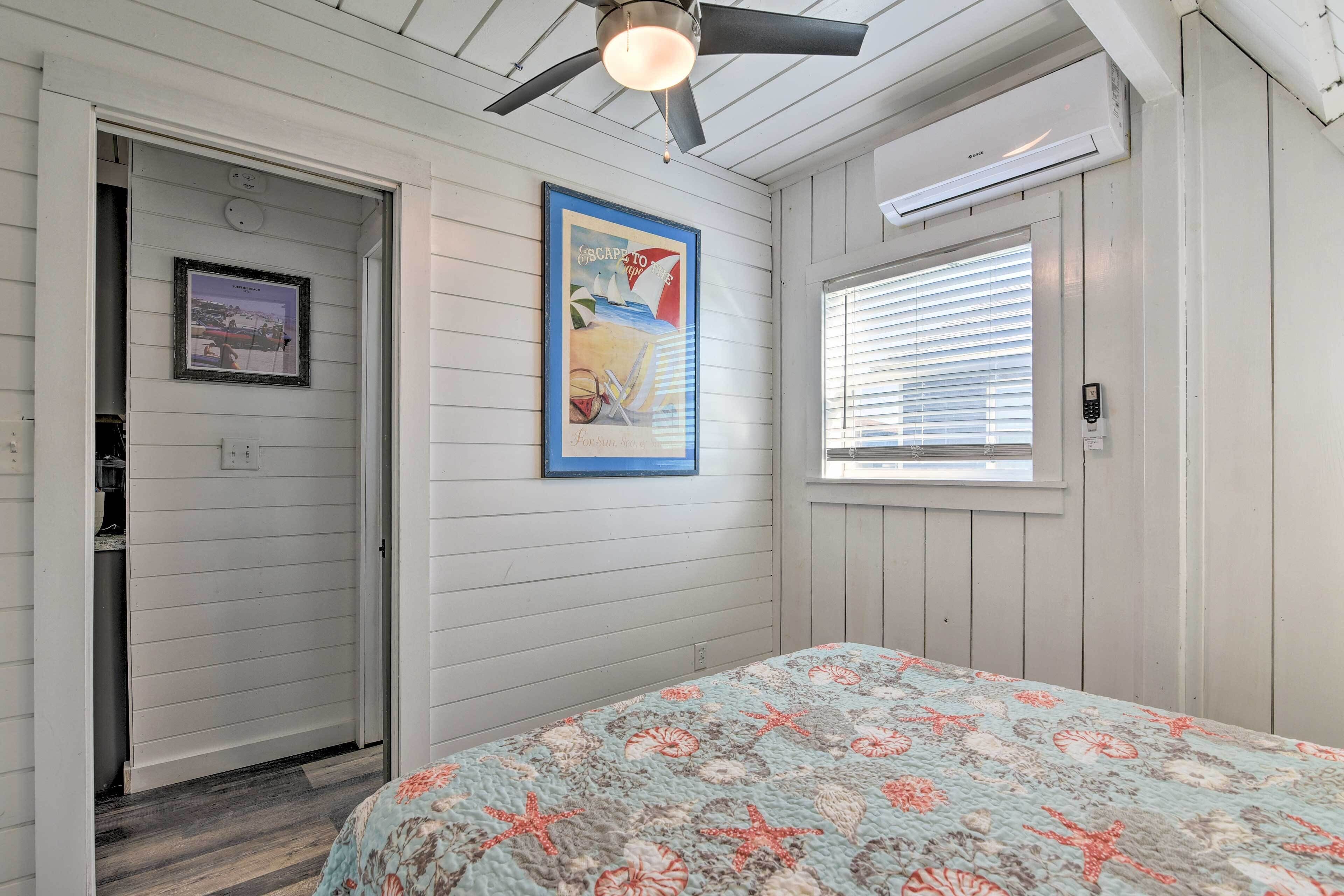 A bedroom with a bed, a ceiling fan, a window with blinds, a framed picture on the wall, and a door.