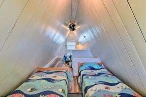 A narrow, sloped room with two beds, a ceiling fan, and a small table. - 2 Blocks to Surfside Beach: A-frame Home w/ Deck (Freeport)
