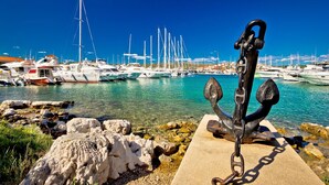 A marina with boats docked, a prominent anchor in the foreground, and rocky terrain. - Seafront apt With Terrace, 4 Bedrooms and Mooring (Rogoznica)