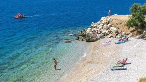 A beach with clear water, a rocky shoreline, and people sunbathing. - Seafront apt With Terrace, 4 Bedrooms and Mooring (Rogoznica)