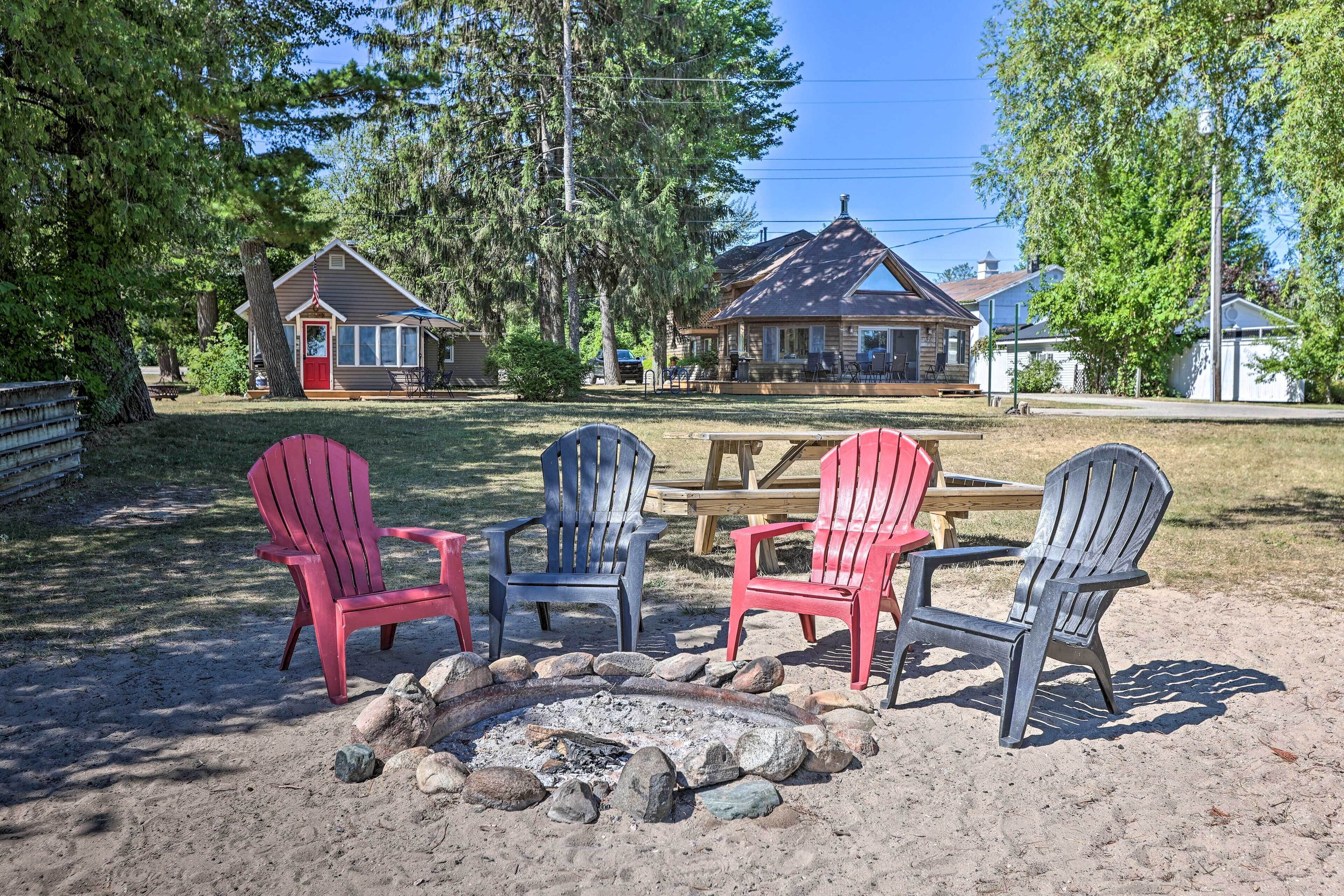 A campsite with a fire pit, red and blue Adirondack chairs, and a picnic table.