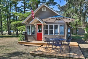 A small cabin with a red door, a deck with outdoor furniture, and an American flag. - 1/2 Mi to Dtwn Suttons Bay! Lakefront Cottage (Suttons Bay)