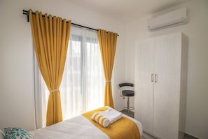 Una habitación de hotel con cama, cortinas, armario y aire acondicionado.