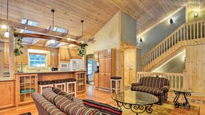 A spacious living area with a wooden ceiling, a kitchen with wooden cabinets, a striped sofa, and a glass coffee table. - 2 Mi to Schuss Mtn! Northern Retreat w/ Game Room (Bellaire)