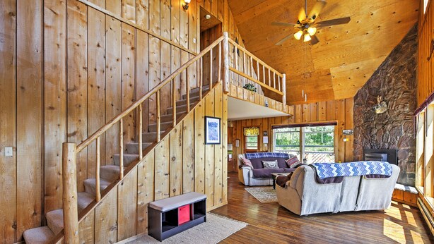 Ein Holzblockhaus-Innenraum mit Treppe, einem Wohnbereich mit Couch und einer Steinwand mit Hirschgeweih.