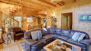 A wooden cabin interior with a leather sectional sofa, a dining area, and a staircase.