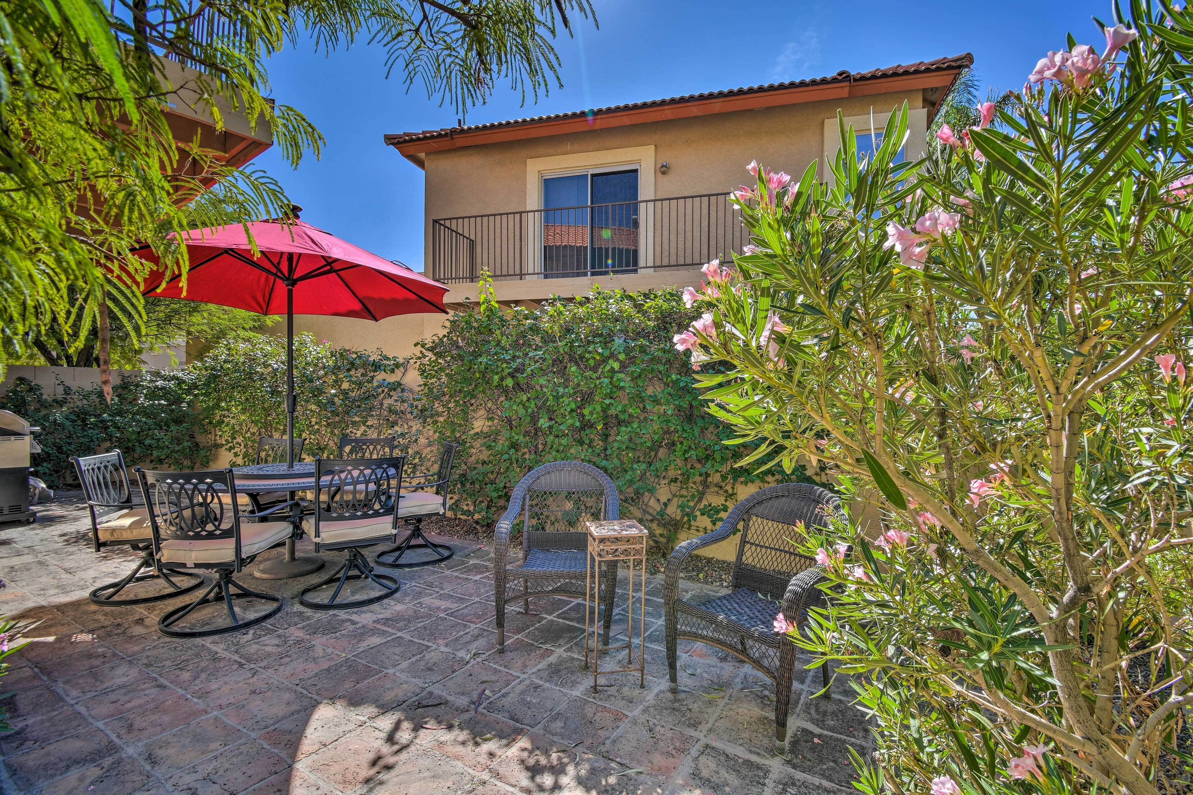 An outdoor patio with a dining table and chairs, a red umbrella, and a building in the background.