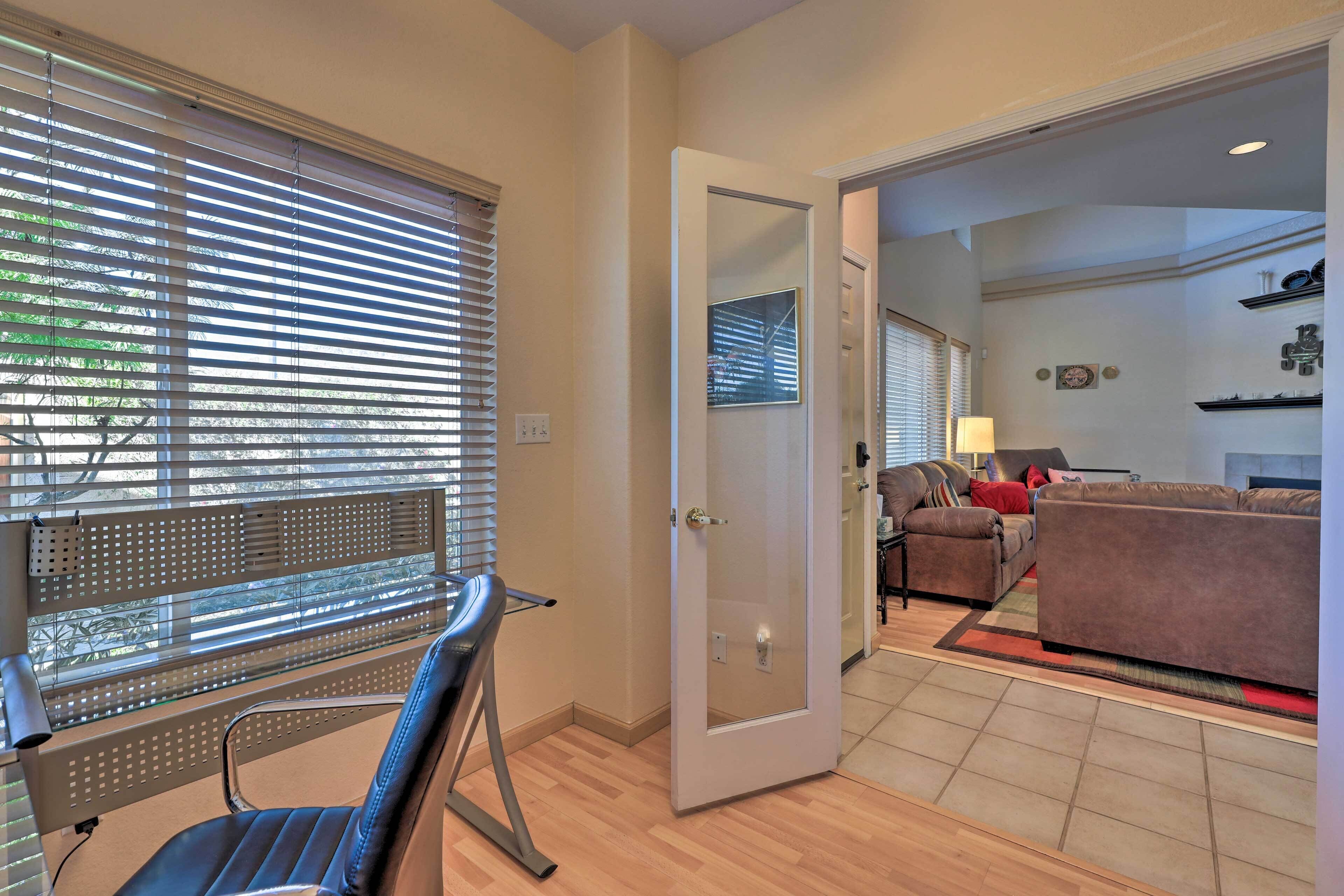 A modern living room with a glass desk, a brown leather sofa, and a glass door leading to another room.