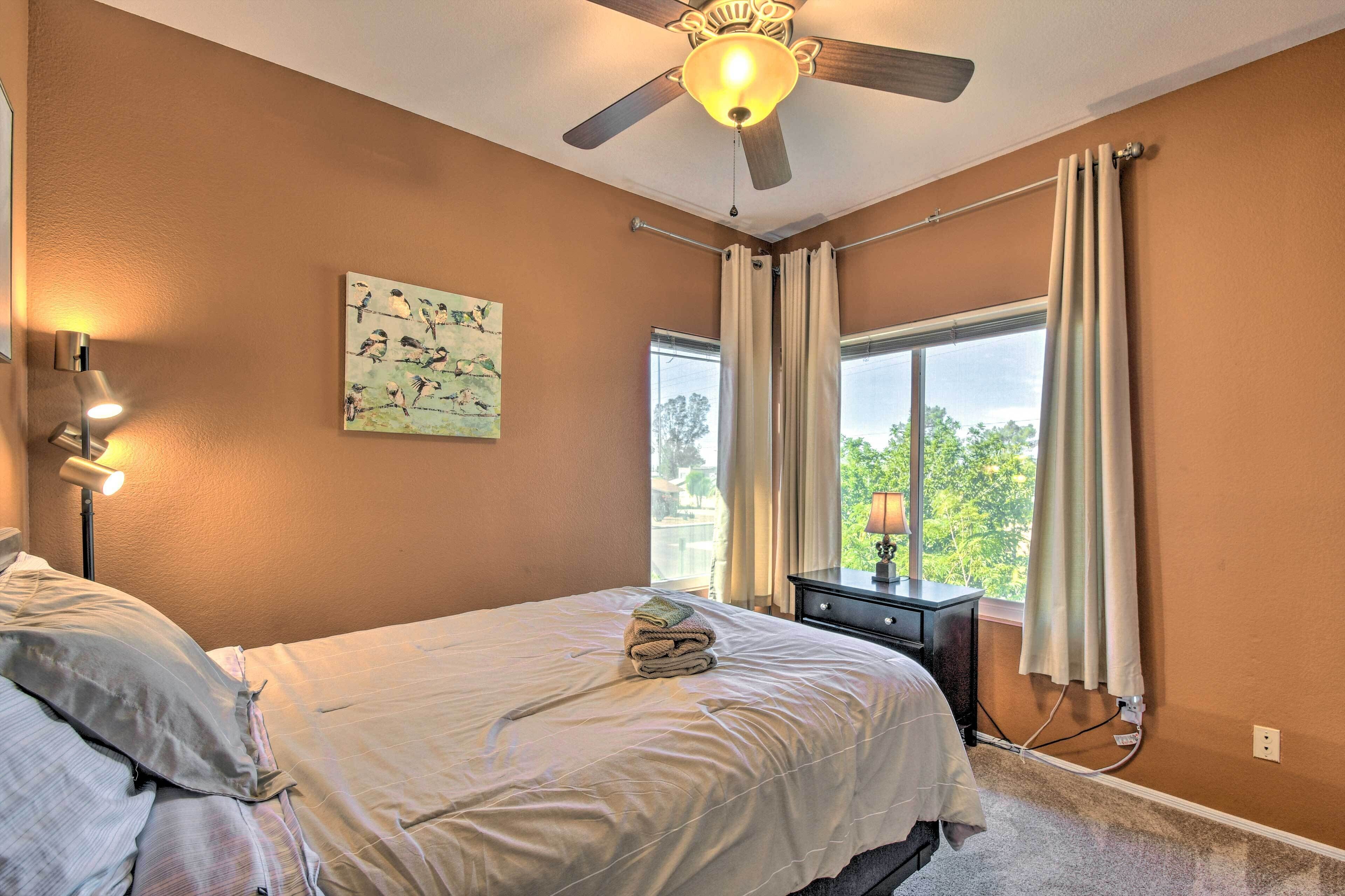 A bedroom with a bed, a ceiling fan, a window with curtains, a nightstand, and a wall-mounted lamp.