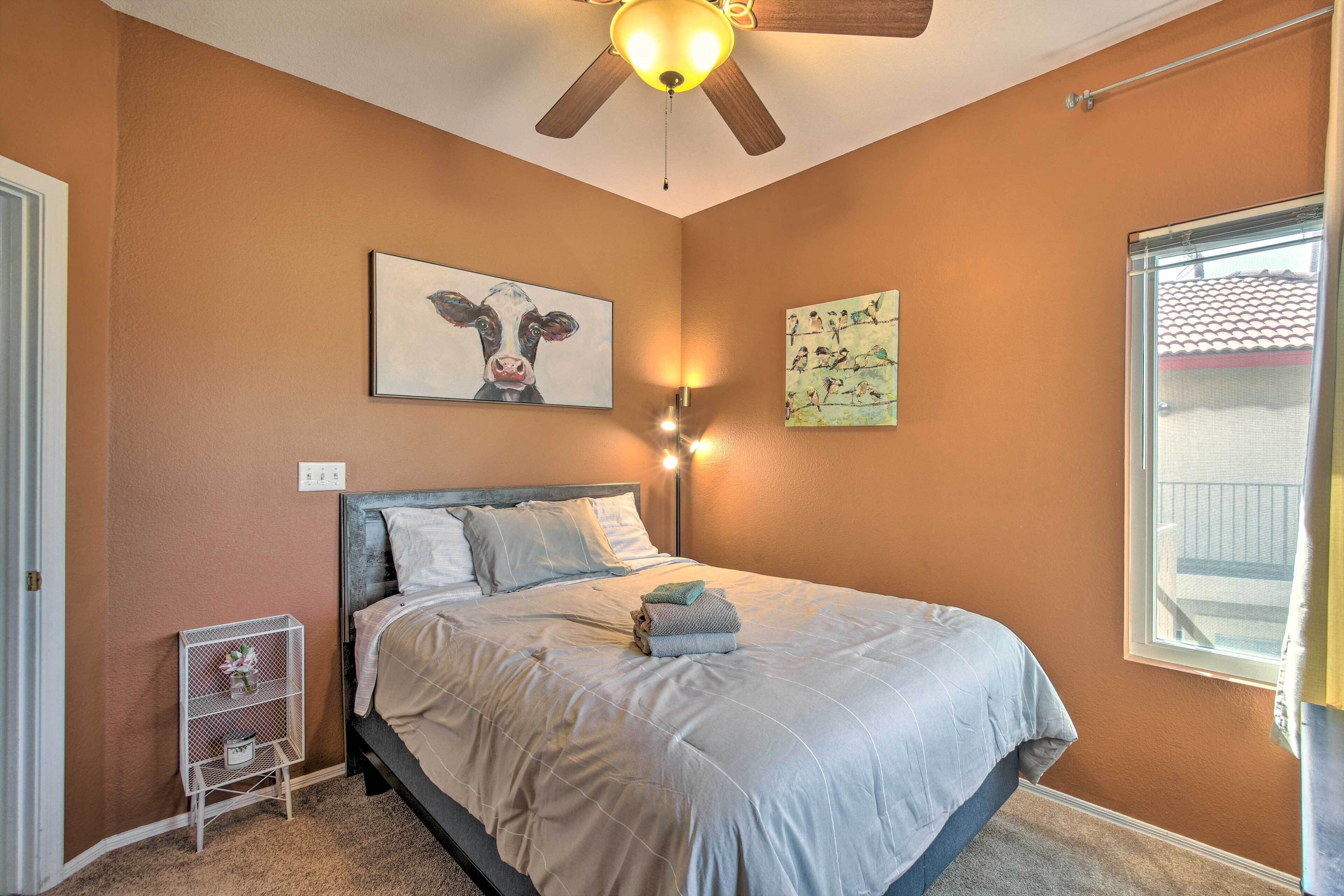 A bedroom with a bed, a ceiling fan, wall art, and a window.