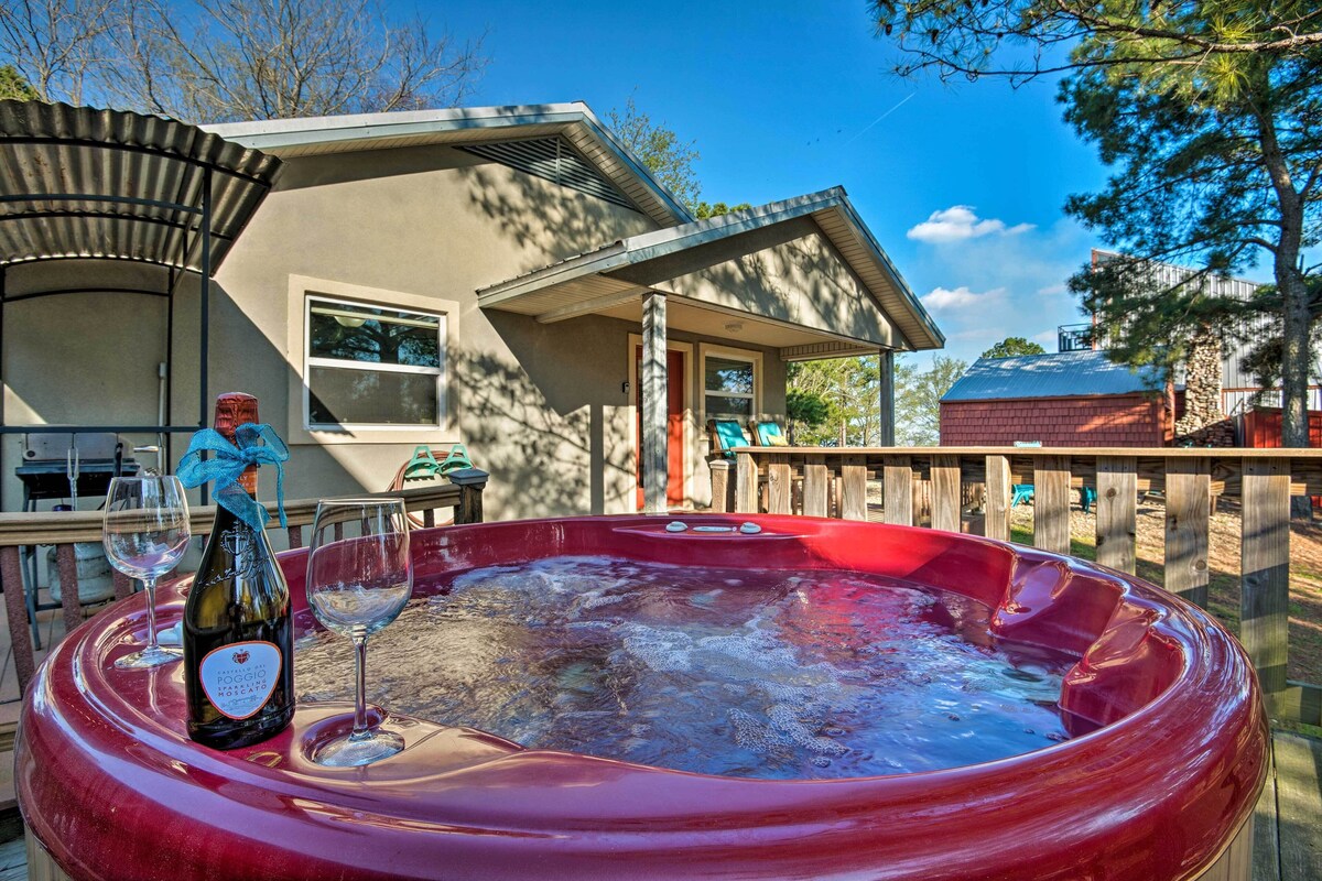 Un jacuzzi con una botella de vino y copas, una terraza de madera y una casa al fondo.