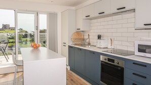 A modern kitchen with a large island, a built-in oven, and a view of a castle through the glass door. - Golygfa'r Gastell / Castle View (Criccieth)