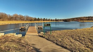 A concrete pathway leading to a wooden dock over a calm body of water, with a green informational sign and a metal railing.