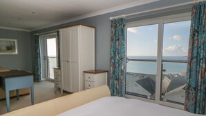 Ein Schlafzimmer mit Bett, Kommode, Schreibtisch und einem Fenster mit Meerblick.