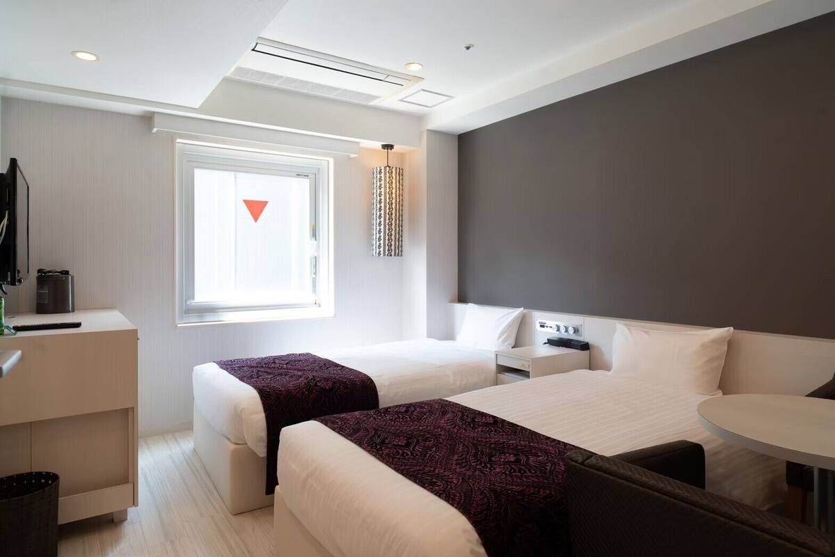 A modern hotel room with two beds, a desk, and a small table.