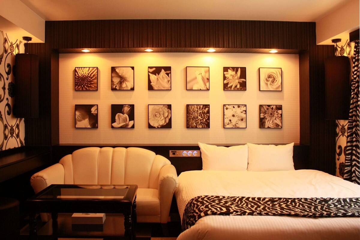 A hotel room with a large bed, a sofa, a table, and a wall decorated with framed artwork.