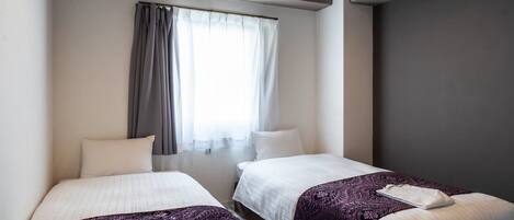 A hotel room with two beds, a window with curtains, and a desk with a lamp.