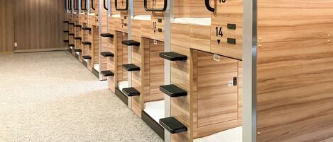 Fila de literas de madera con compartimentos numerados, suelo alfombrado y pared de madera.