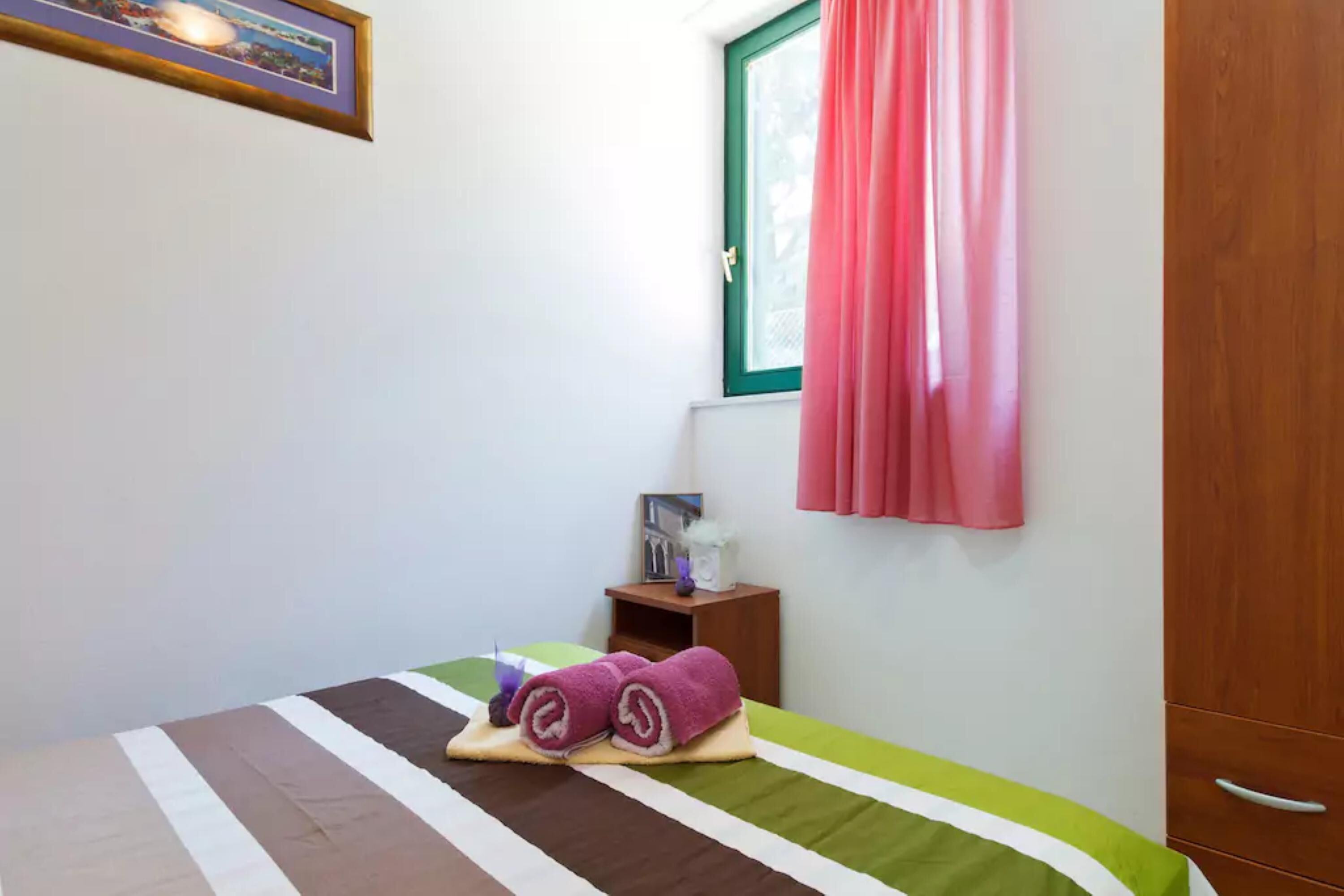 A neatly made bed with striped bedding and a rolled towel on a small bedside table.