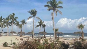 Una playa con palmeras y sombrillas de paja.