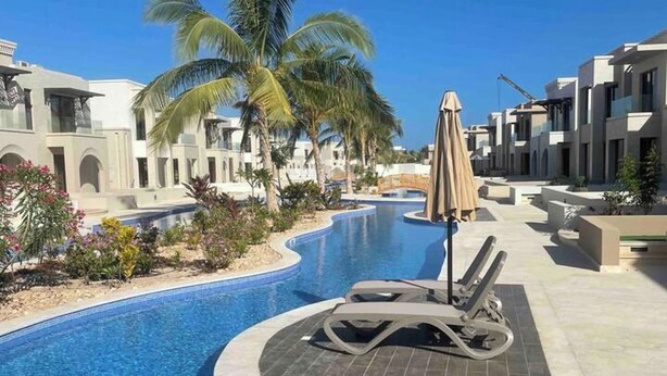 Una piscina con sillas de descanso, palmeras y edificios modernos.