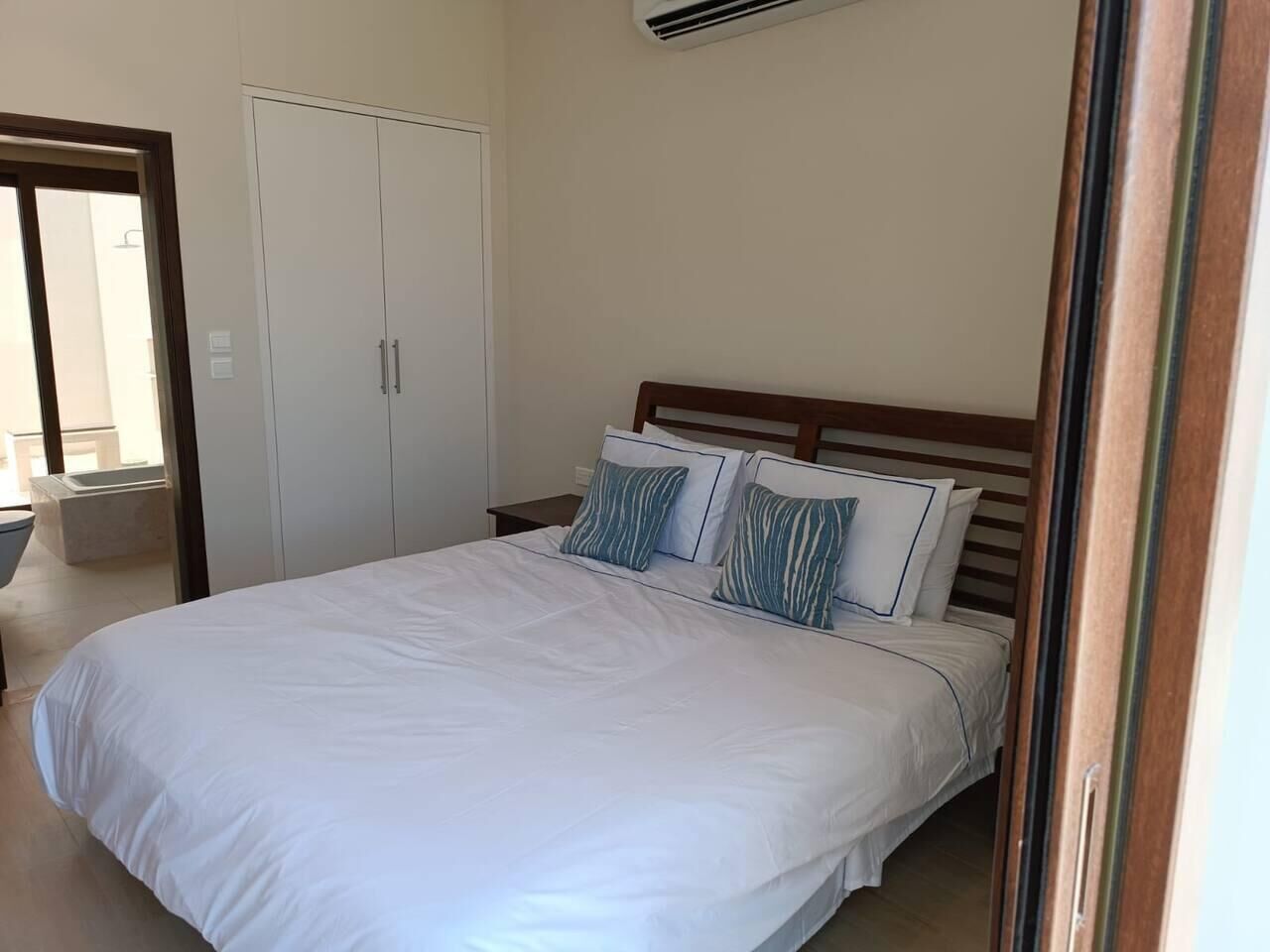 A bedroom with a large bed, two bedside tables, a wardrobe, and an air conditioning unit.