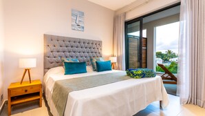 A bedroom with a large bed, a nightstand, a window with a view of palm trees, and a balcony with a chair. - Charming 2-Bed Apartment in Grand Baie (Grand Baie)