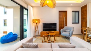 A modern living room with a sofa, a television, a wicker hanging light fixture, and a blue bean bag. - Charming 2-Bed Apartment in Grand Baie (Grand Baie)