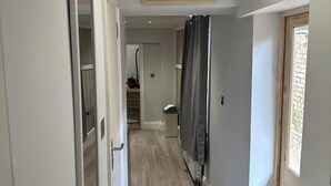 A narrow hallway with a wooden floor, a door on the left, and a window on the right. - 1-Bed - Sleeps 2 - Acton Park & Stn Close (London)