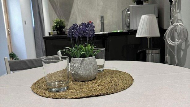 A dining table with a woven placemat, two clear glasses, and a stone planter with purple flowers. - 1-Bed - Sleeps 2 - Acton Park & Stn Close (London)