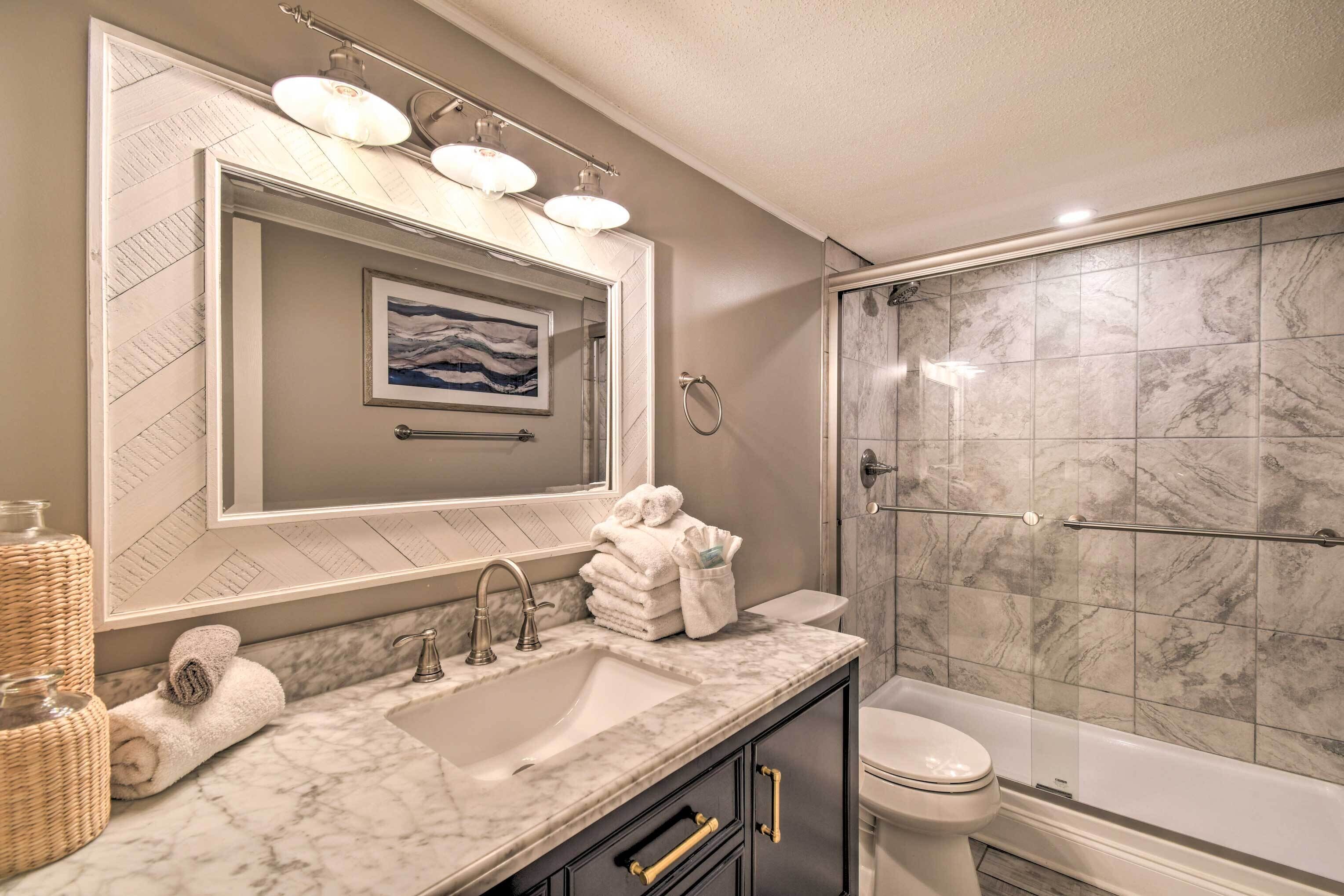A bathroom with a marble sink, a large mirror, a framed picture, and a glass-enclosed shower.
