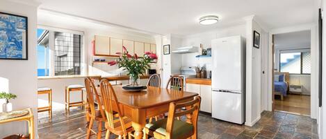 A modern kitchen with white cabinets, a central island, and a dining area with wooden chairs and a table.