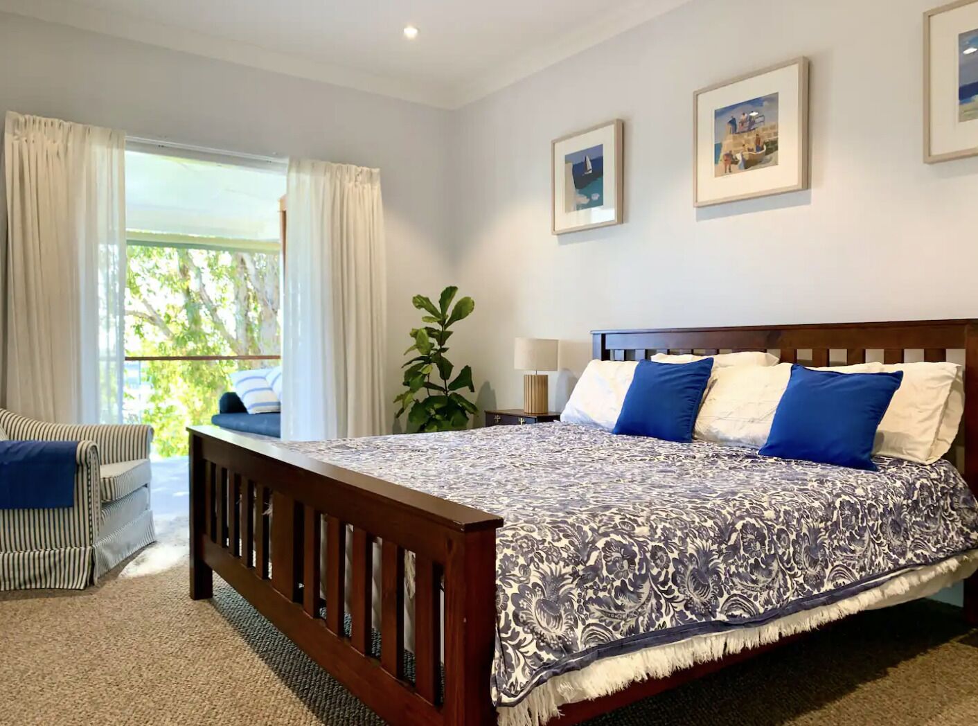 A bedroom with a bed, a window with curtains, a plant, and two framed pictures on the wall.
