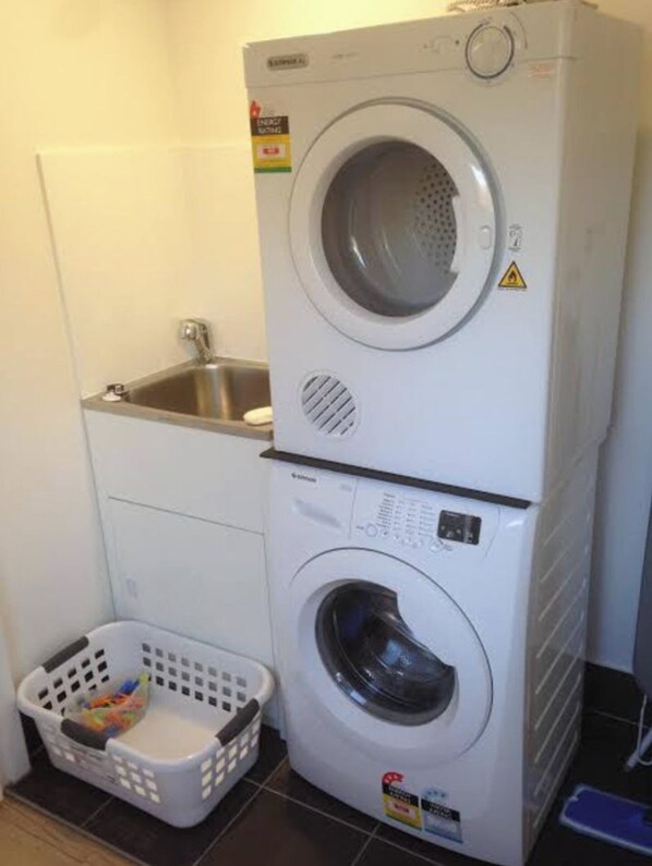 A stacked washer and dryer unit with a small sink and a laundry basket. - LUXURY HAVEN! Beautiful, central, wifi & spacious! Walking to everything! (Yamba)