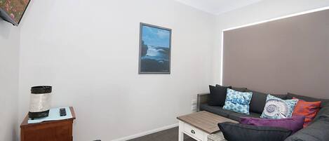 Una sala de estar moderna con un sofá gris, una mesita de madera, un control remoto y un marco de fotos en la pared.