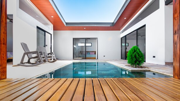 A modern indoor pool area with wooden decking, lounge chairs, and a glass door leading to a bedroom. - Coral House, 5 min to the beach-  fiber optic internet and swimming pool  (Uvita)