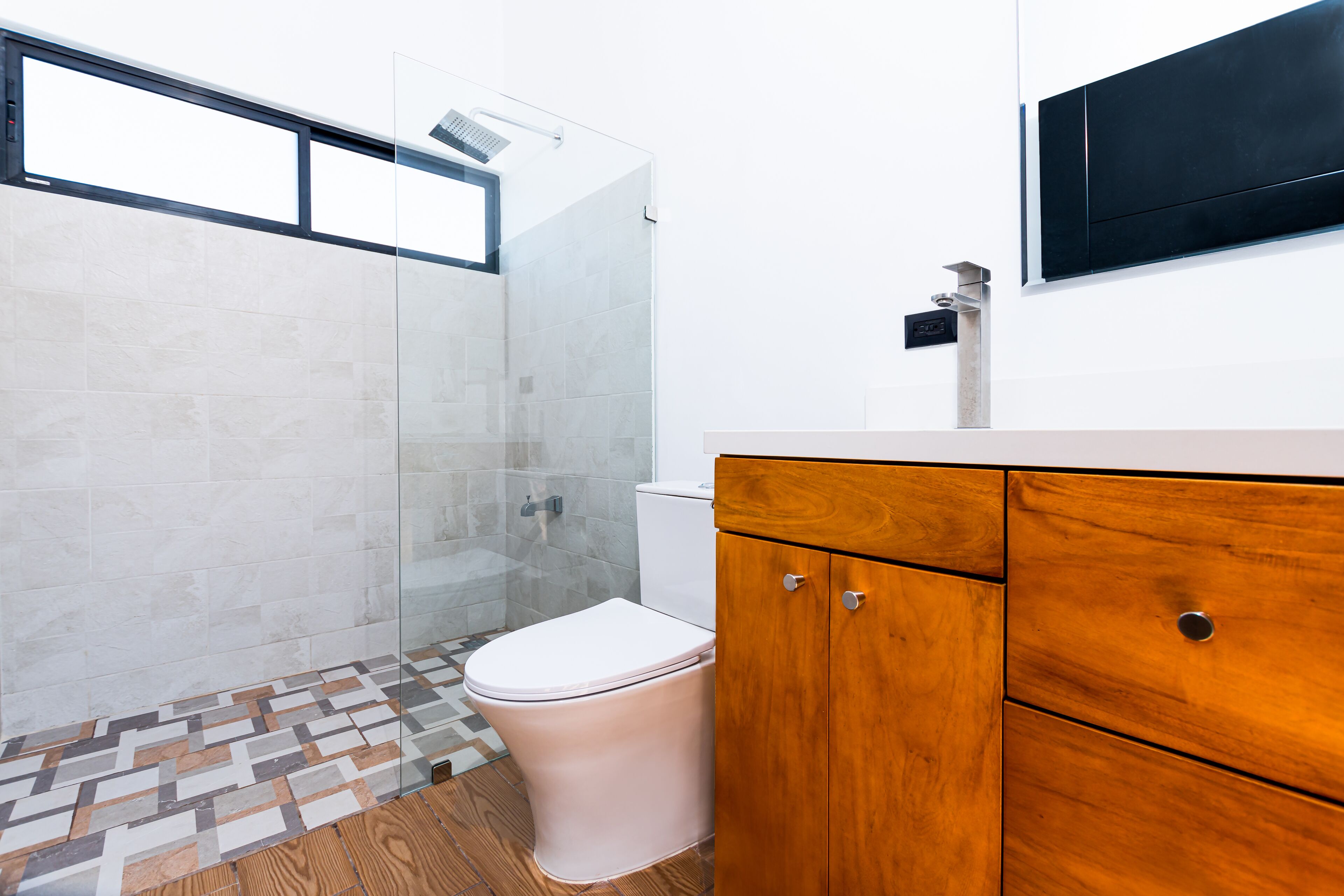 A modern bathroom with a glass shower enclosure, a white toilet, and wooden cabinetry.