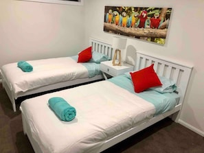 Two single beds with red pillows and a framed picture of parrots adorn this simple hotel room.